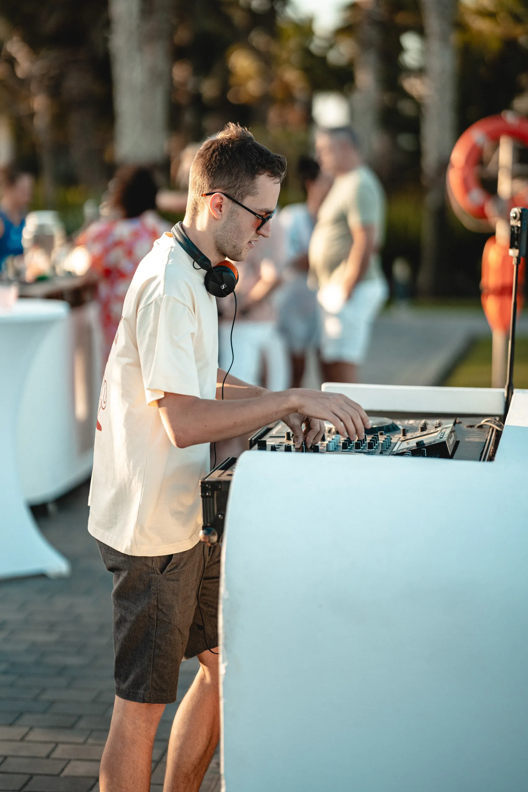 DJ Moritz am weißen Pult, Hochzeitsgäste stehen am Pool