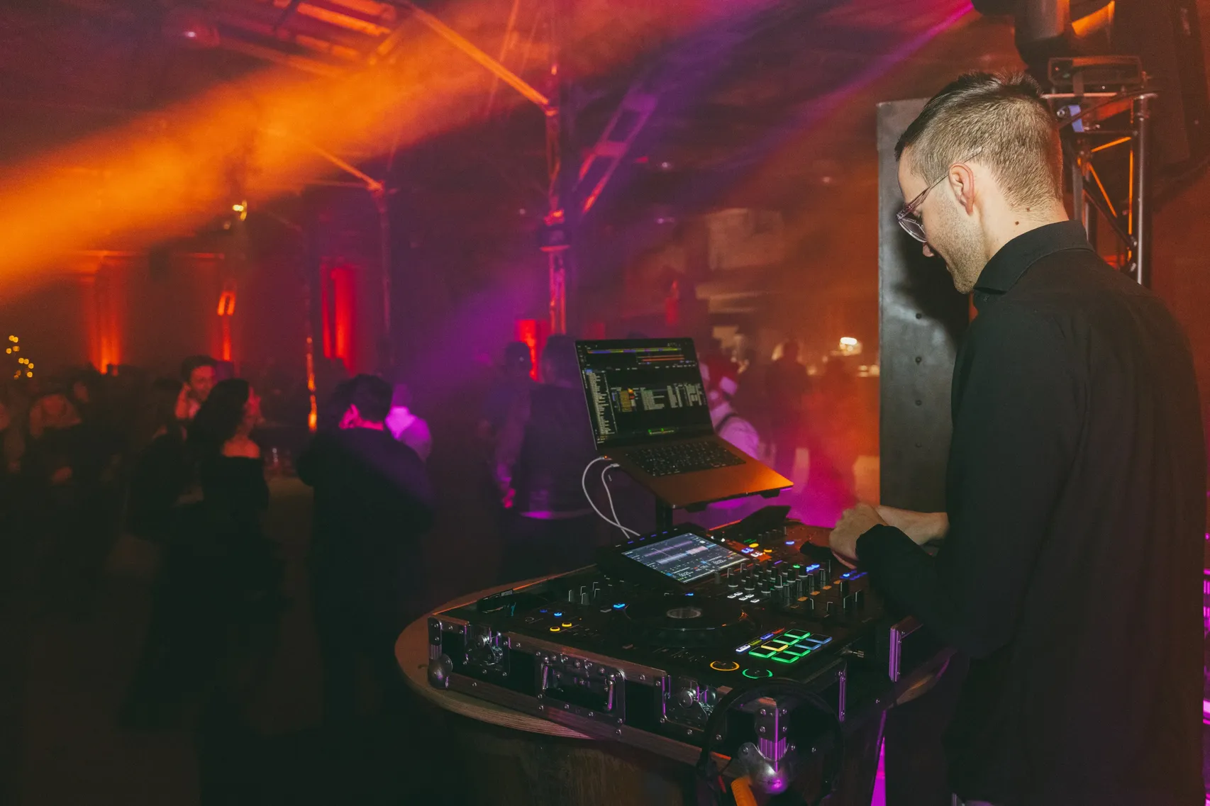 DJ Moritz Gräßler lächelt am DJ-Pult, hinter ihm leuchtet die Tanzfläche orange