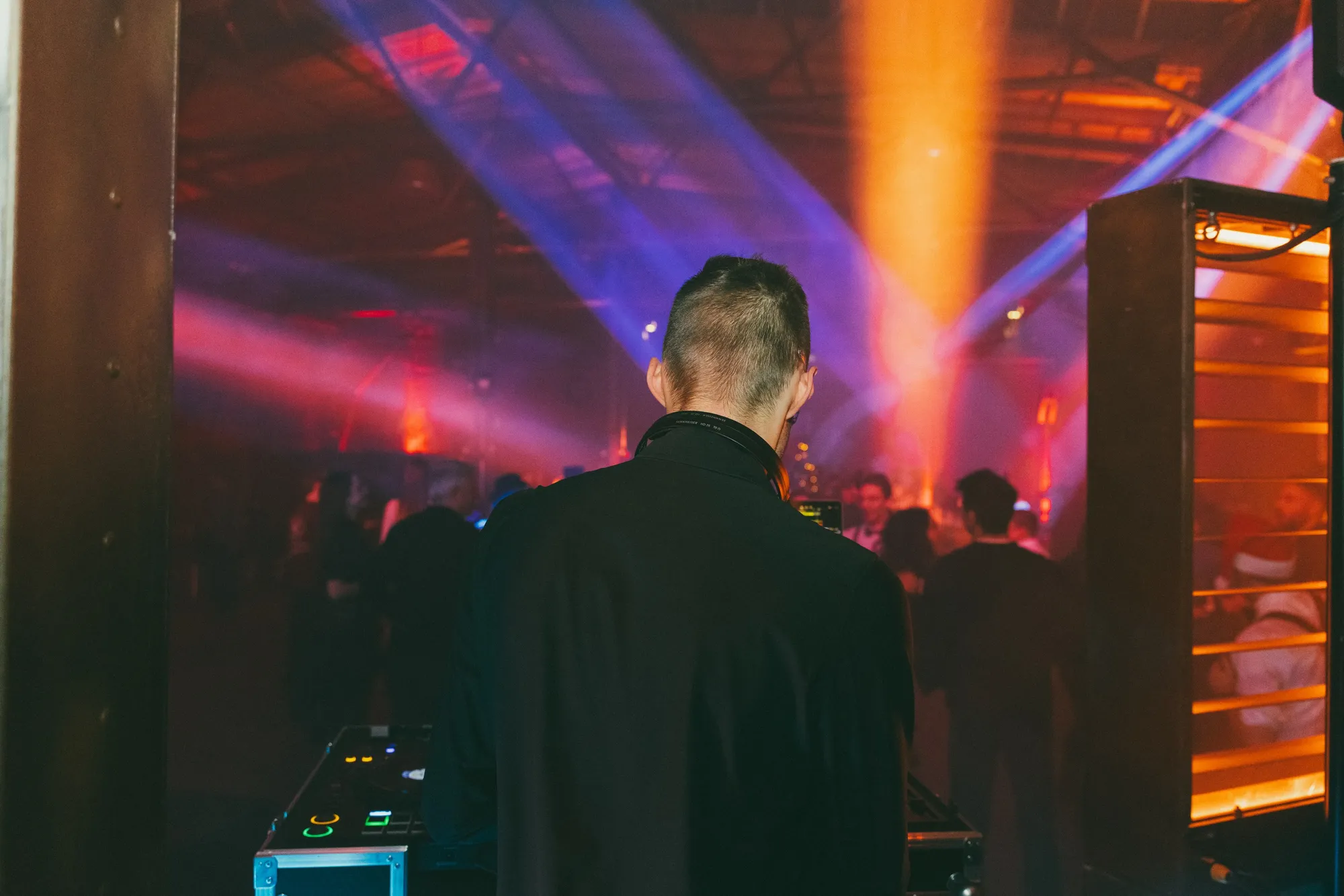 DJ Moritz von hinten am Pult, vor ihm feiert das Publikum im bunten Licht