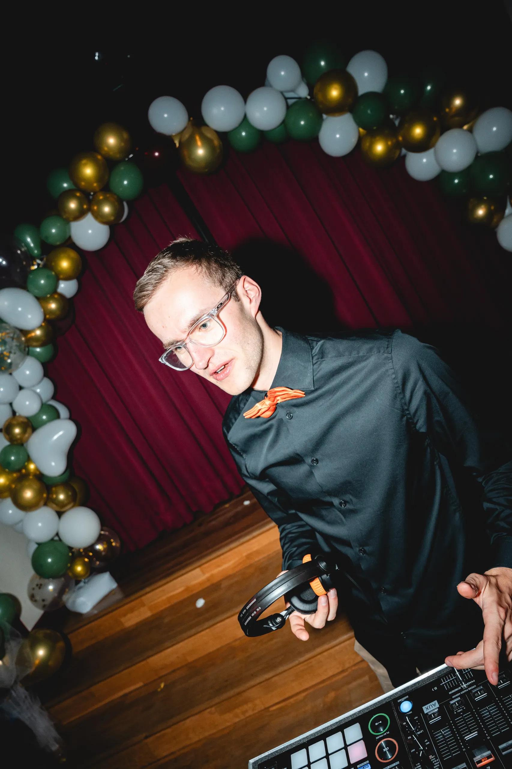 Hochzeits-DJ Moritz lacht am DJ-Pult, hinter ihm ein Ballonbogen auf einer Hochzeit