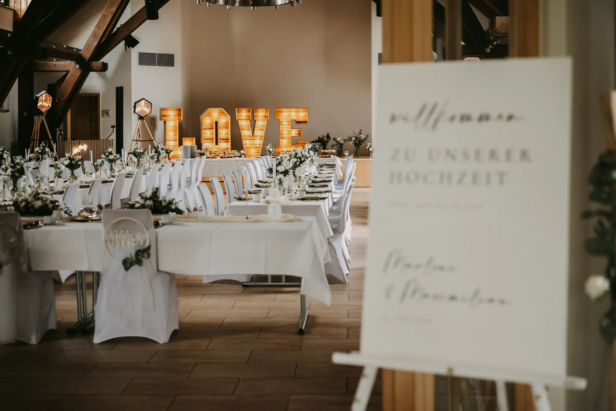 Hochzeitsraum mit weißen Tafeln, LOVE-Buchstaben und Begrüßungsschild